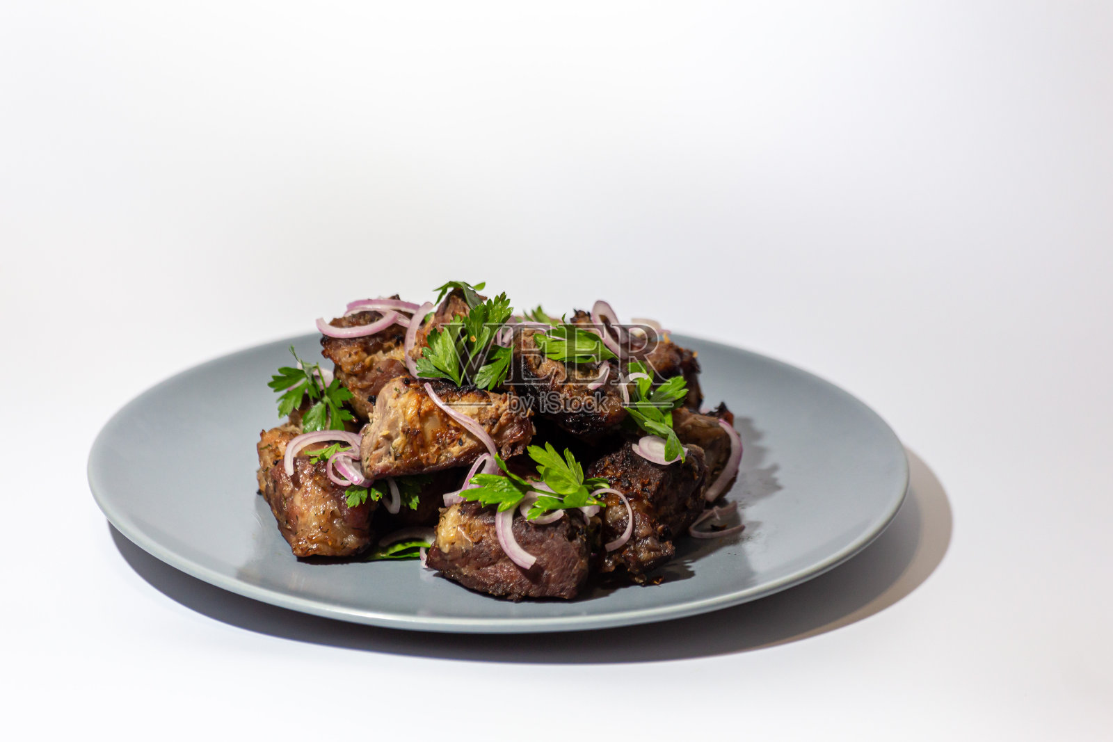 羊肉串——猪肉片和葱、香草一起在木炭上煎，放在石板托盘上，背景是白色的。照片摄影图片