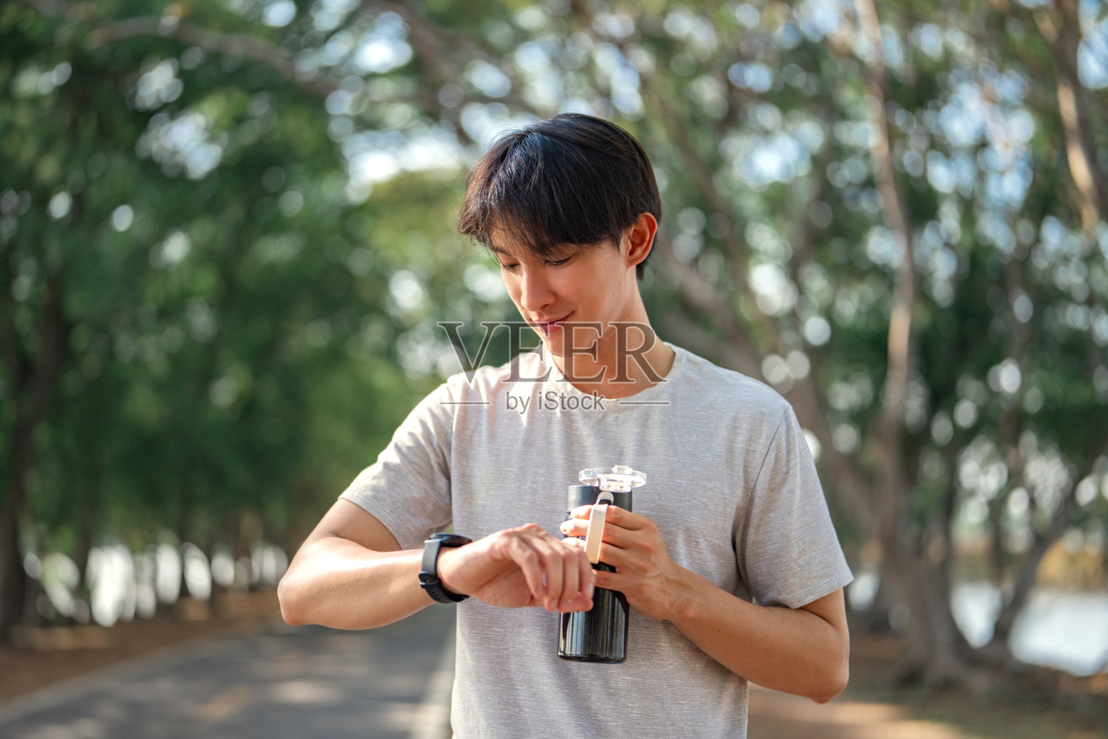 ชื่อผลงาน:快乐的亚洲人与smartwatch运动员检查他的运行时间,水瓶在公园户外。为了健康和健康而锻炼和训练。照片摄影图片