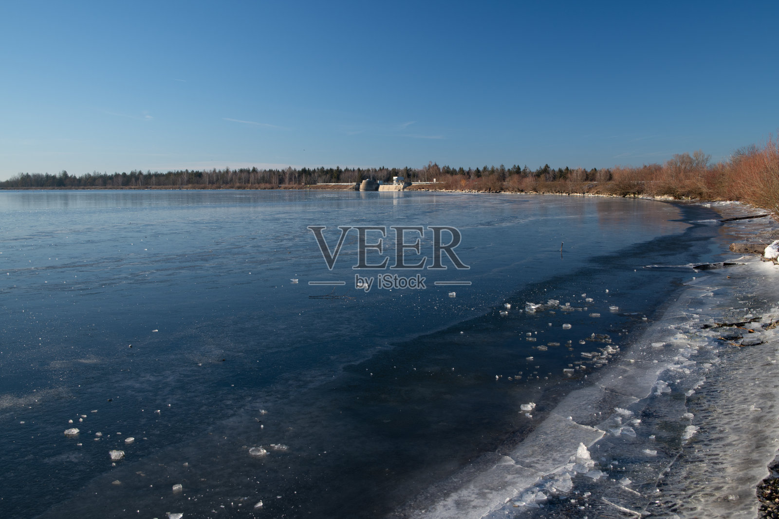 蔚蓝的天空映衬着冰封的大湖。背景中的水闸。边缘的冰部分破碎了。照片摄影图片