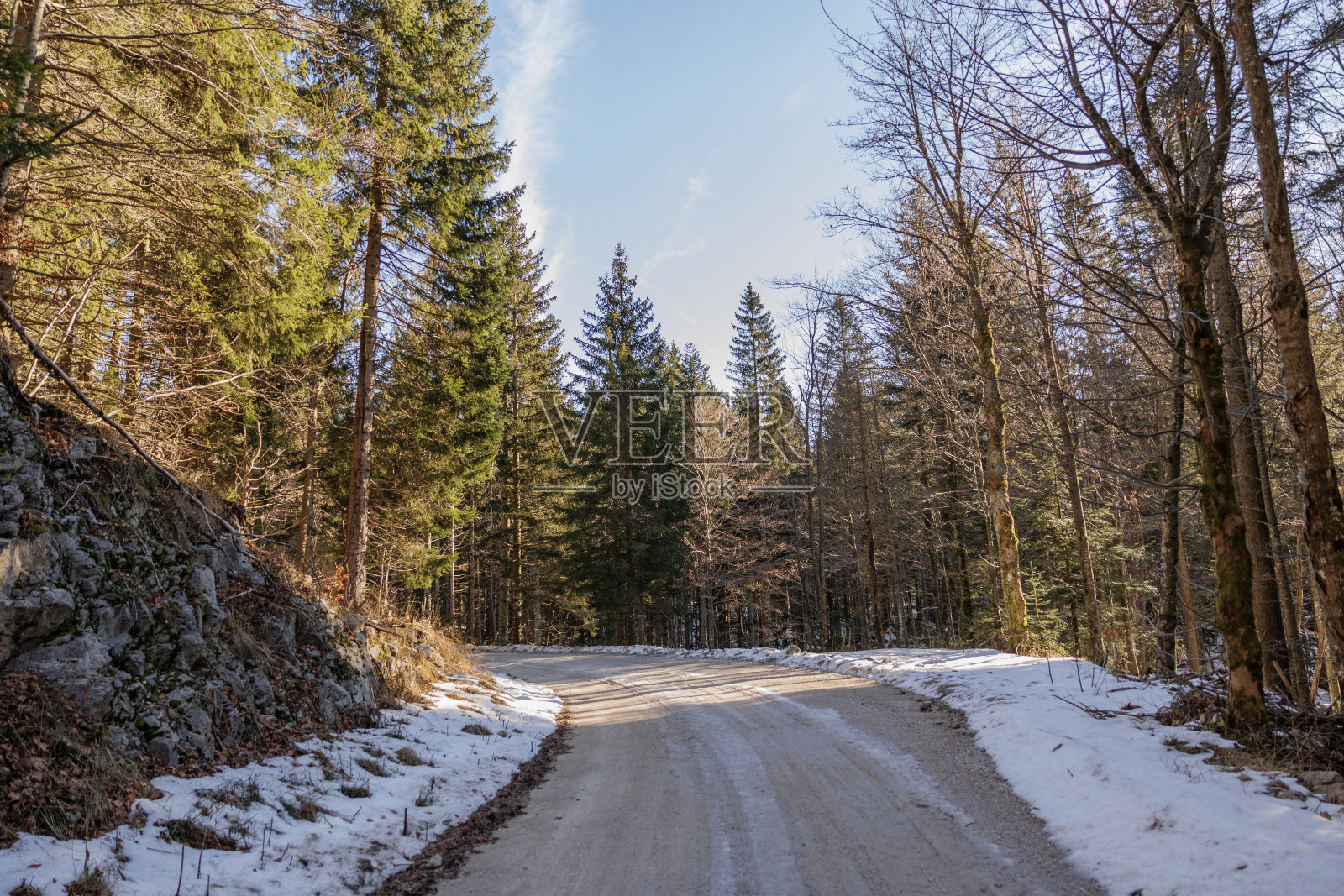 一条土路的全景，部分结冰，被雪覆盖，穿过斯洛文尼亚的山林中央，在晴朗的天空下，在冬天，早晨晚些时候的阳光部分照亮了这条路照片摄影图片