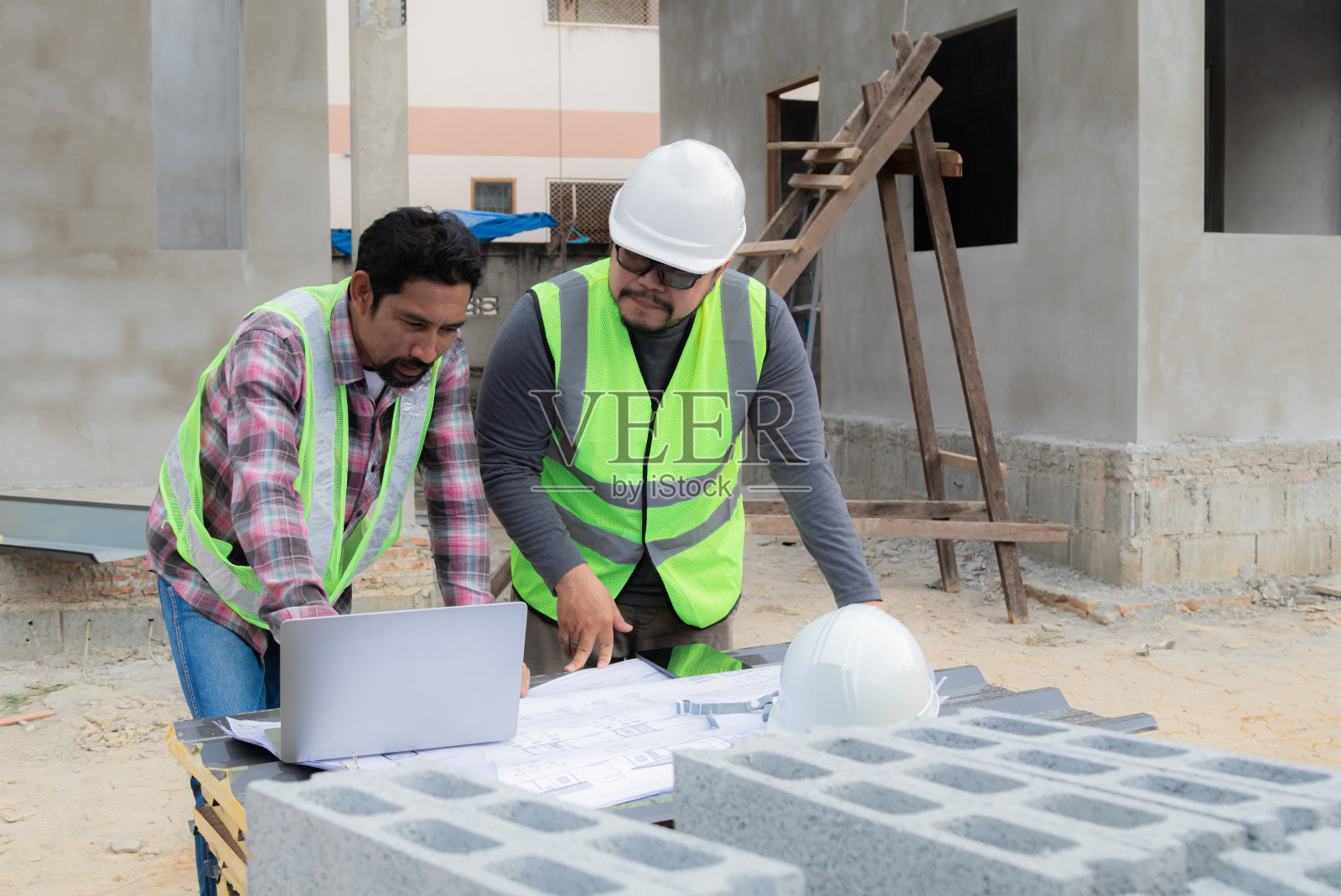 年轻的超重工程领班与亚洲或印度承包商合作项目经理在户外工地阅读蓝图文件，使用笔记本电脑技术解决问题照片摄影图片