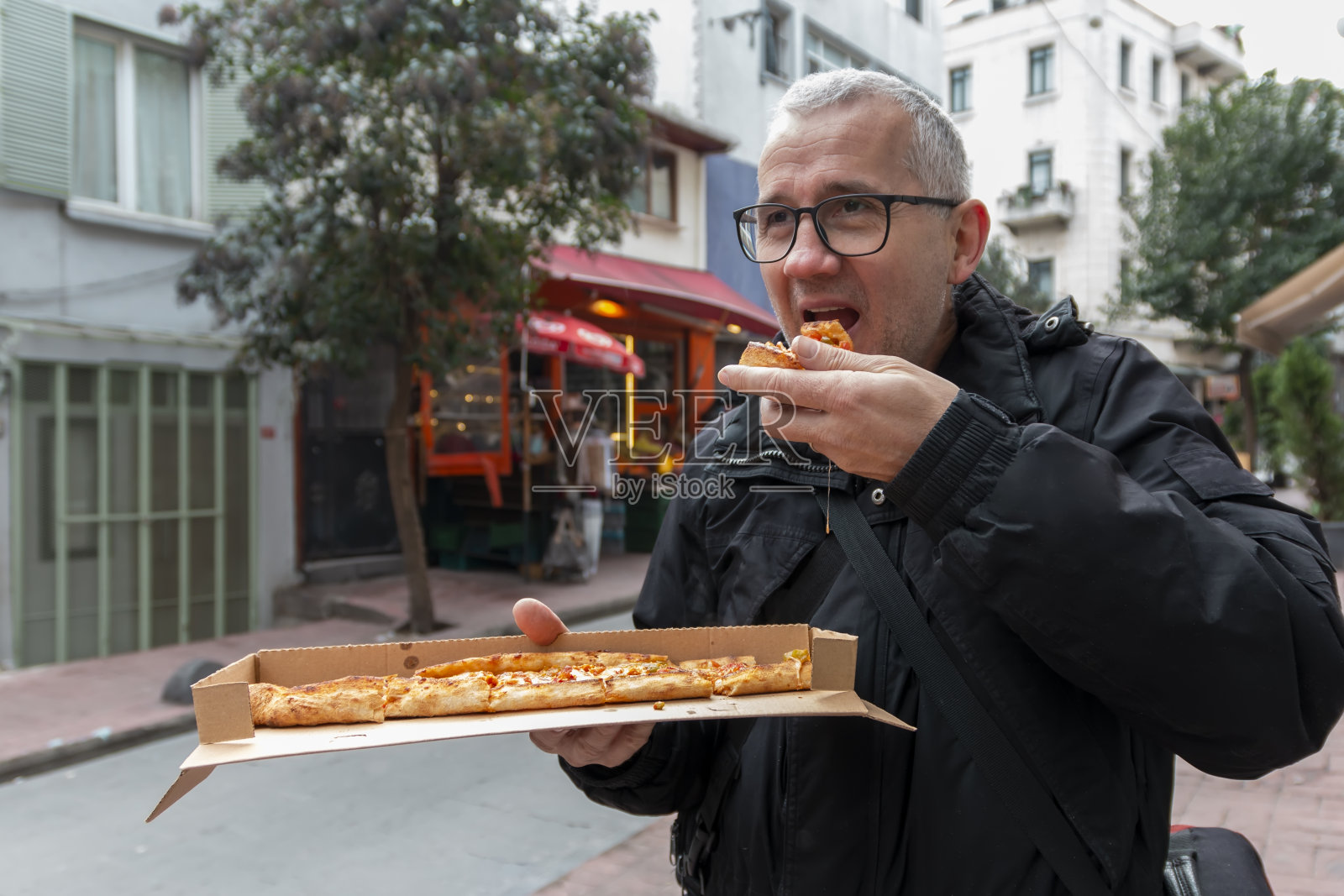 一个成熟的独自旅行者正在吃盒子里的披萨。照片摄影图片