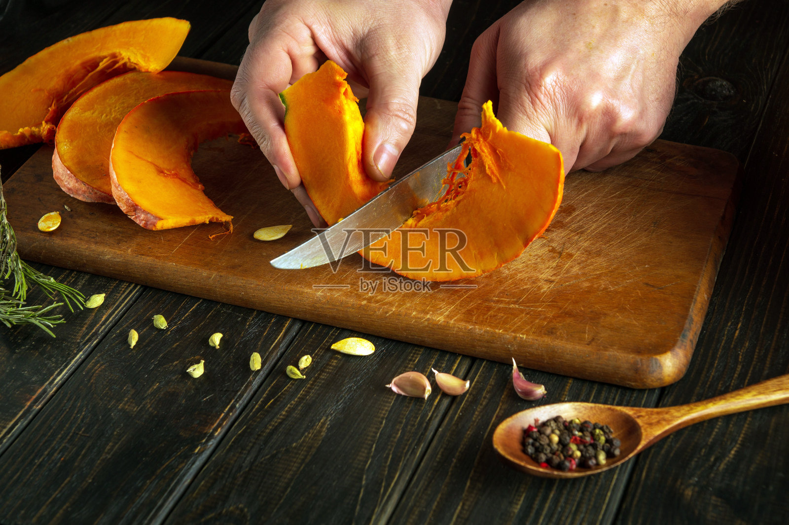 厨师的手用刀在厨房板上切一片南瓜。为美味的派准备食材的概念照片摄影图片