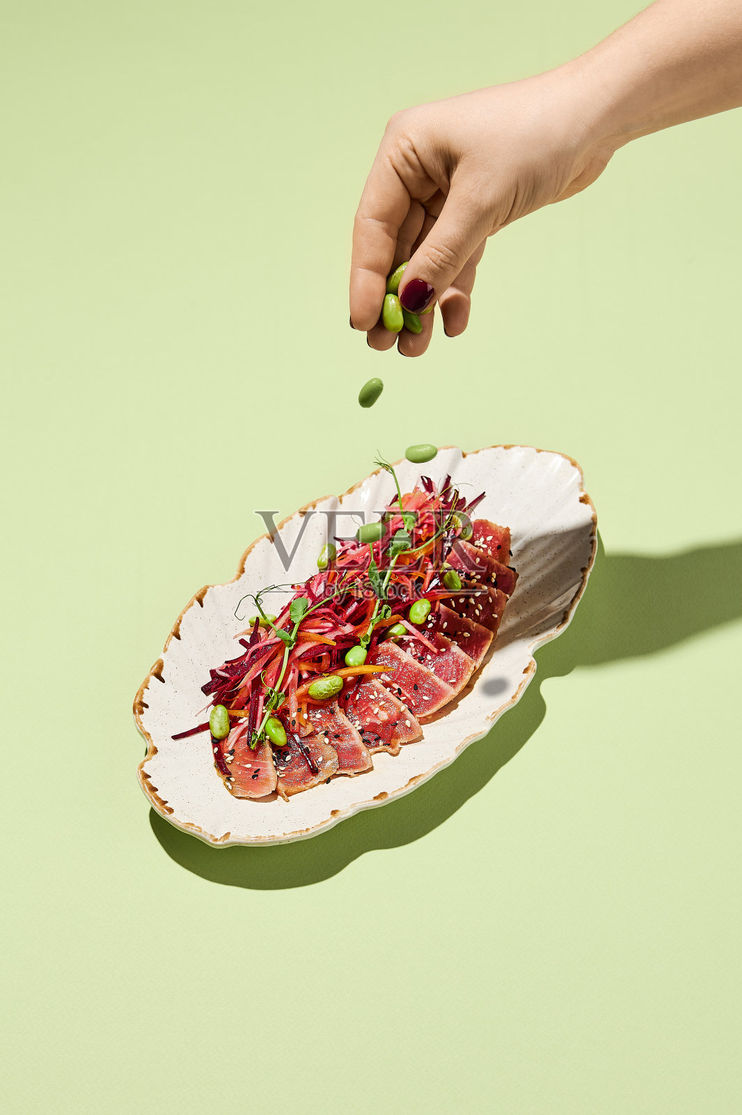 一名妇女用手将青豆撒在金枪鱼tataki和蔬菜沙拉上，这是一种健康概念的代表照片摄影图片