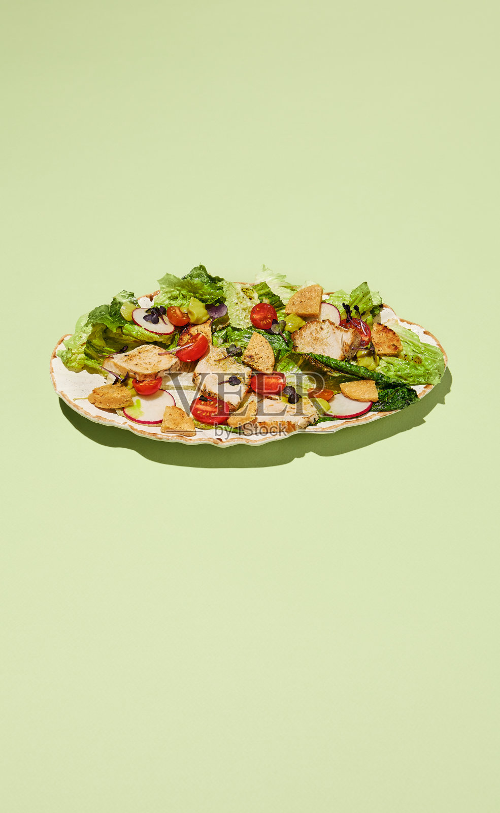 健康的凯撒沙拉或火鸡配上各种蔬菜和烤面包，放在一个手工制作的盘子里，背景是柔和的绿色照片摄影图片