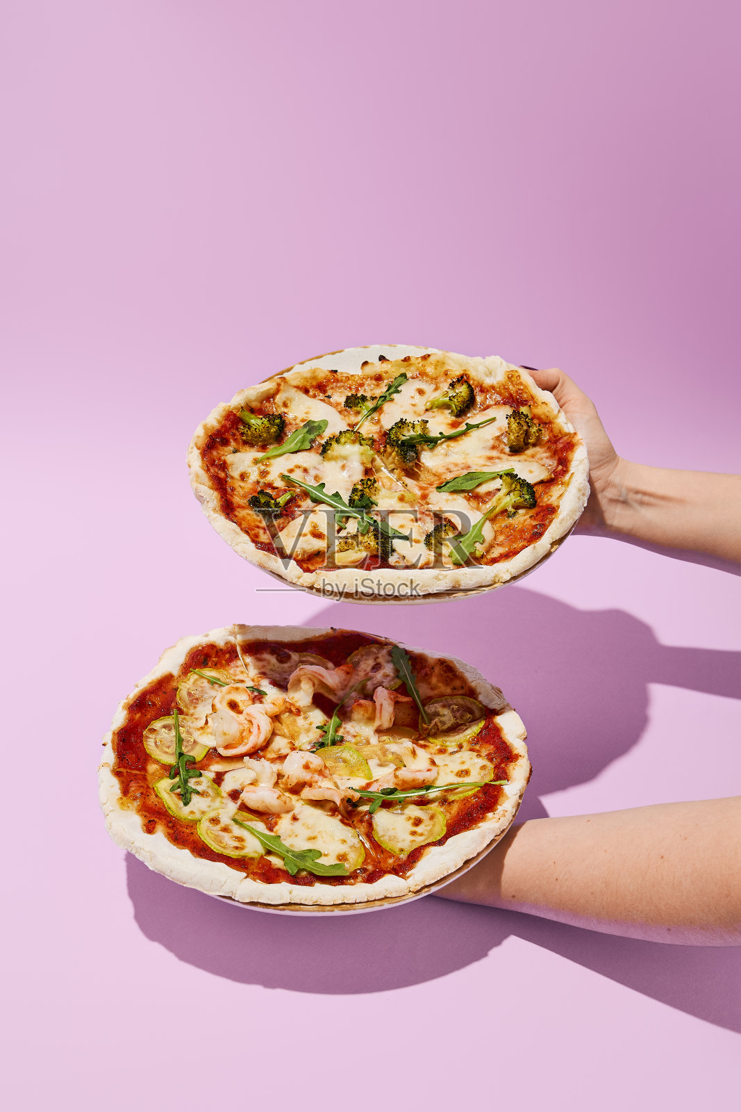 女人的手拿着两个健康的无麸质披萨，紫色背景上的简约风格照片摄影图片