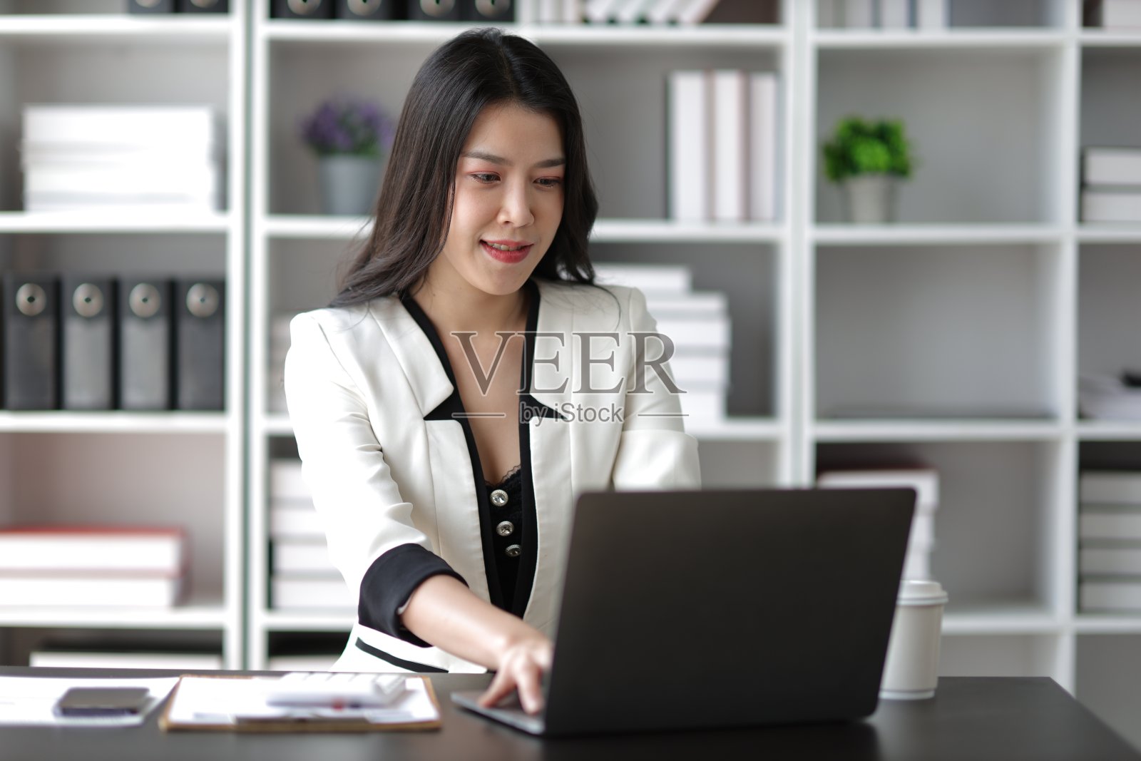 迷人的亚洲女商务秘书，在办公室里用笔记本电脑和文书工作。照片摄影图片