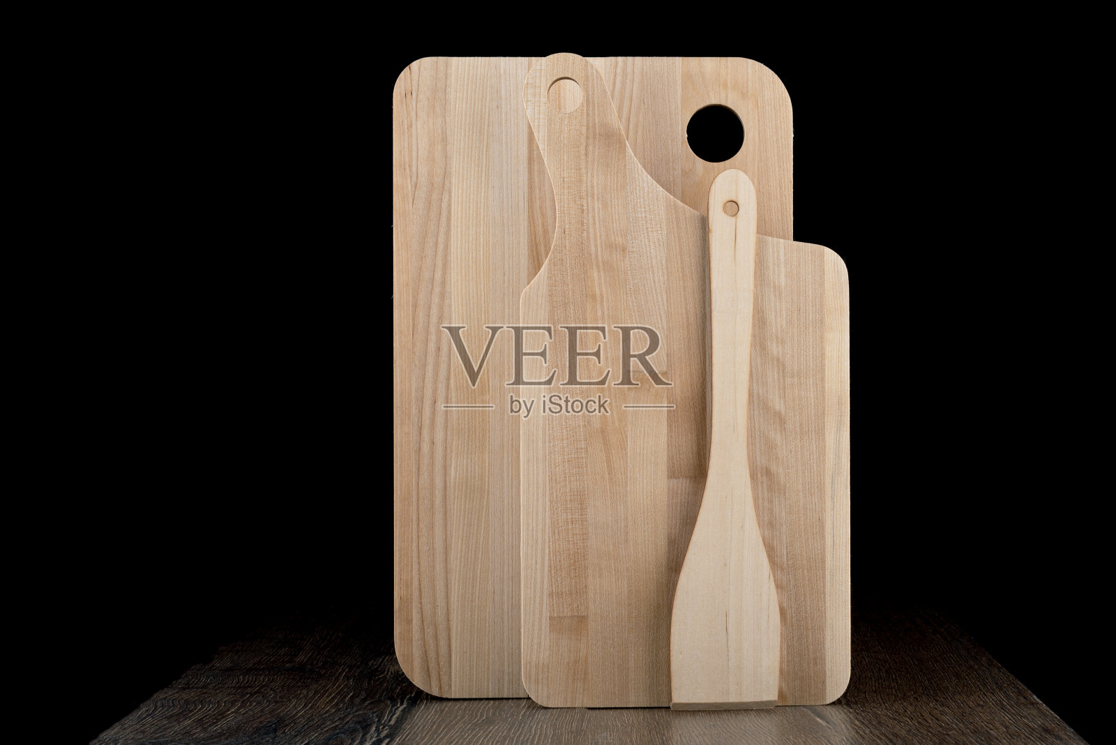 一套新的木制砧板和厨房用的木制刮刀，背景是黑色的。照片摄影图片