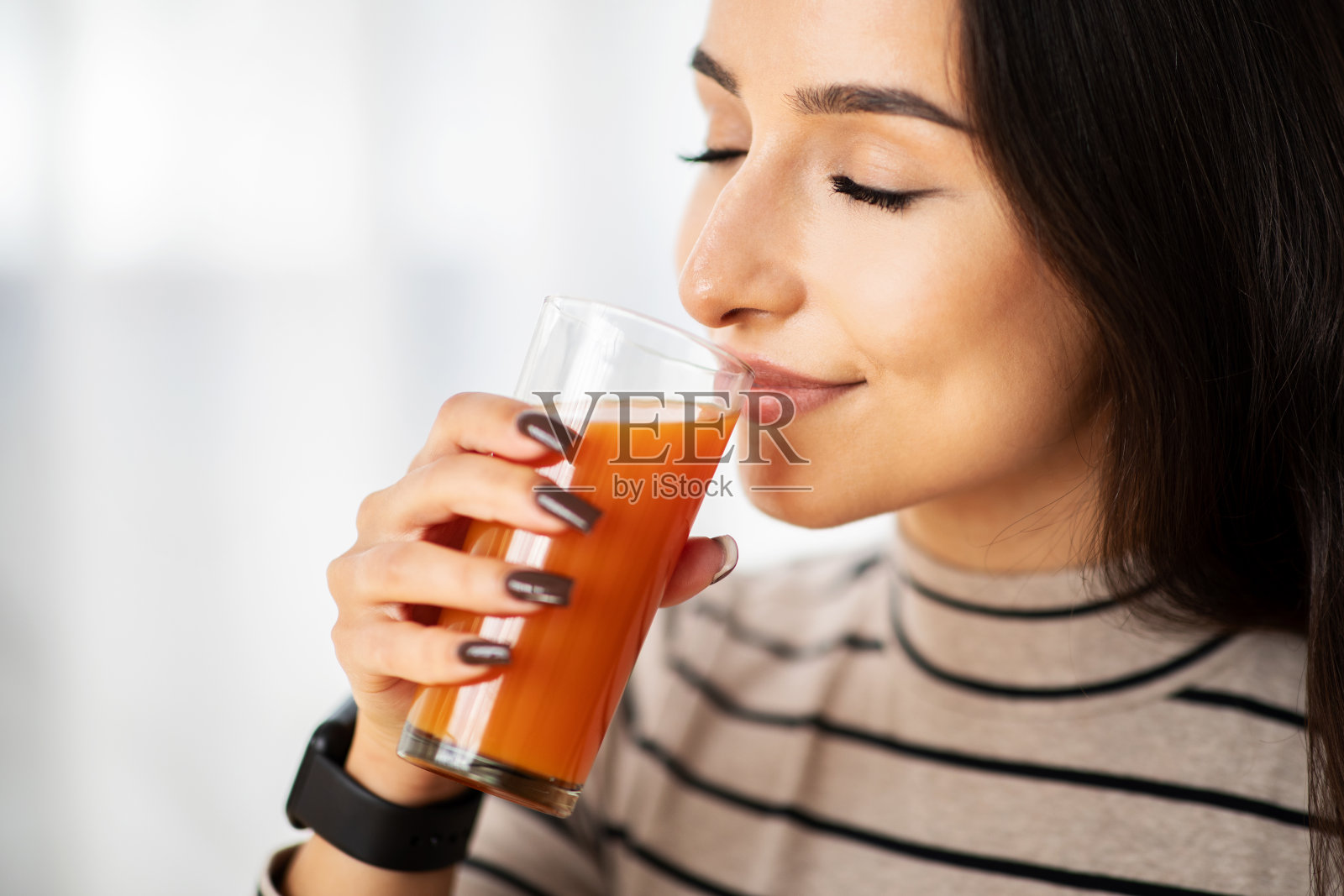 快乐的年轻阿拉伯女子在房间里喝着一杯新鲜可口的果汁，靠近照片摄影图片
