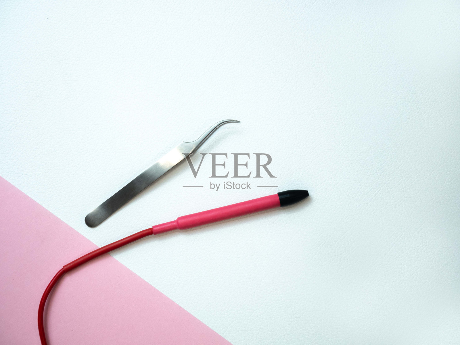 电脱毛工具在粉红色的背景与文字的地方。一个电动脱毛器手柄，一个装着电极的针，镊子。去除多余的体毛照片摄影图片