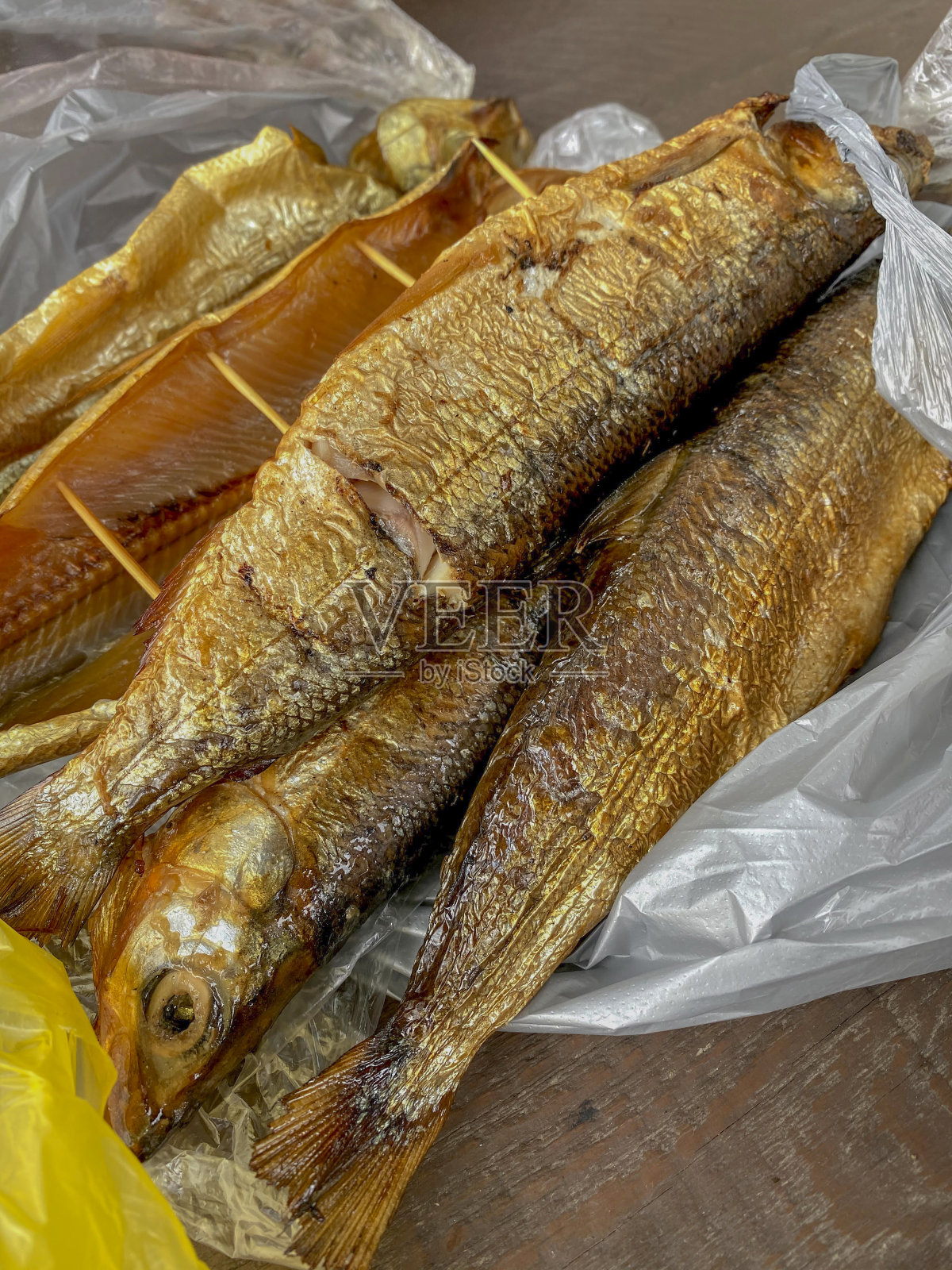 木桌上装着塑料袋的熏鱼。前视图。照片摄影图片