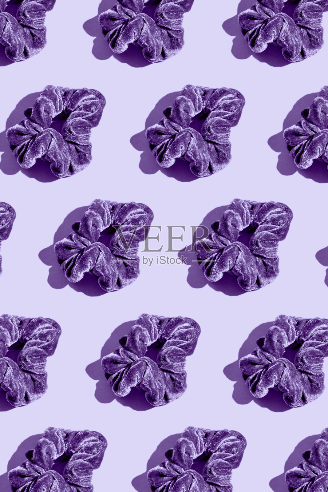 在柔和的背景上用紫色头发橡皮筋做成的创意图案。最小的风格照片摄影图片