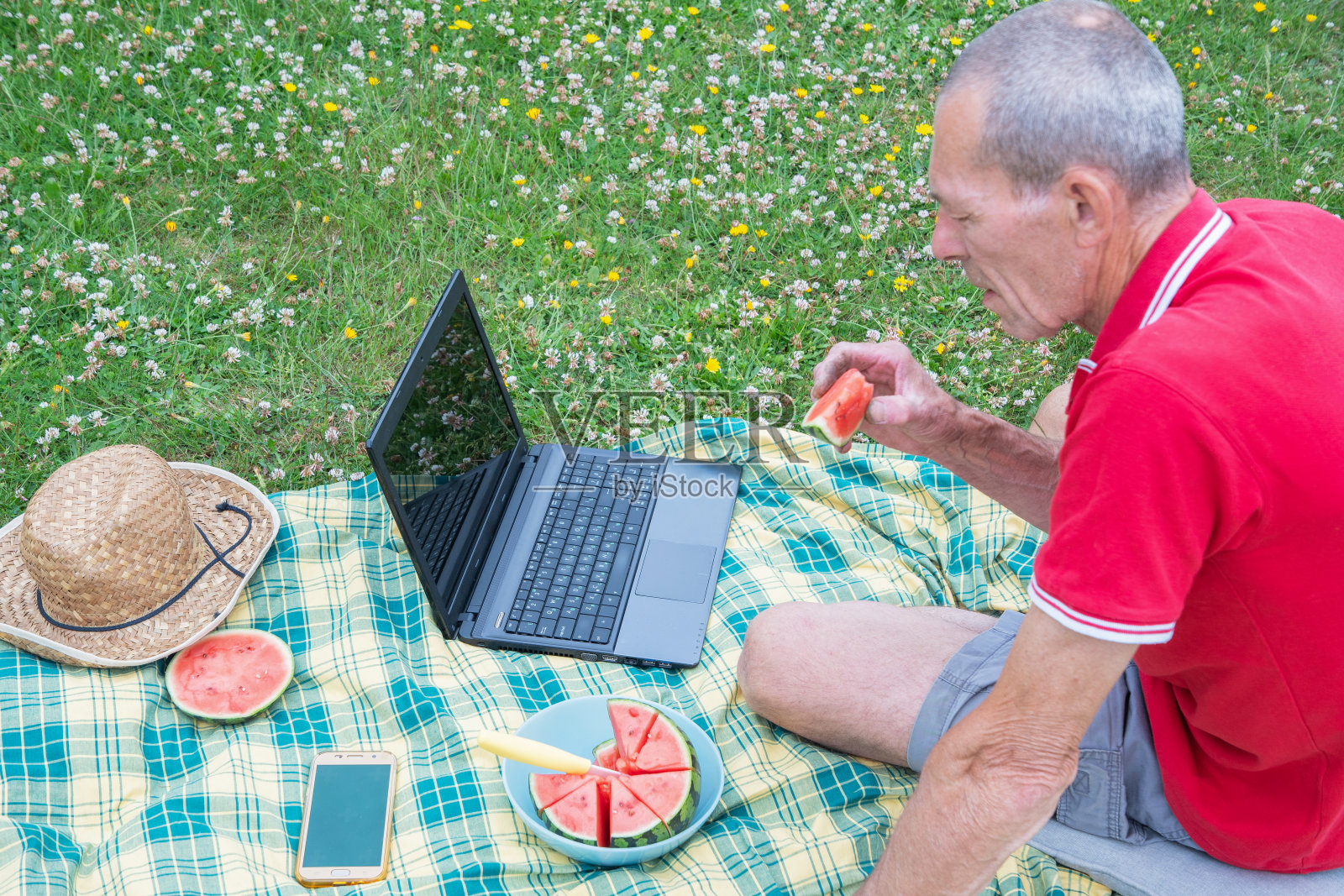 一名拿着手机和笔记本电脑的中年男子躺在绿草地上的毯子上照片摄影图片