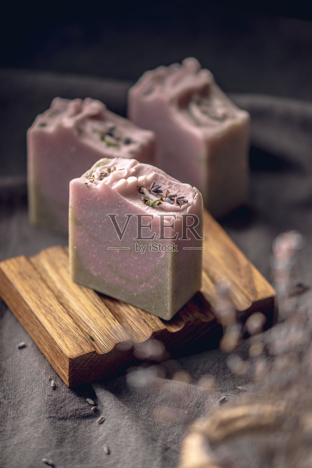 一块块天然薰衣草手工肥皂，放在木制肥皂盘上，在深色织物背景上，上面有干花。有机化妆品的概念，一个有用而有趣的爱好，一张美丽的明信片照片摄影图片