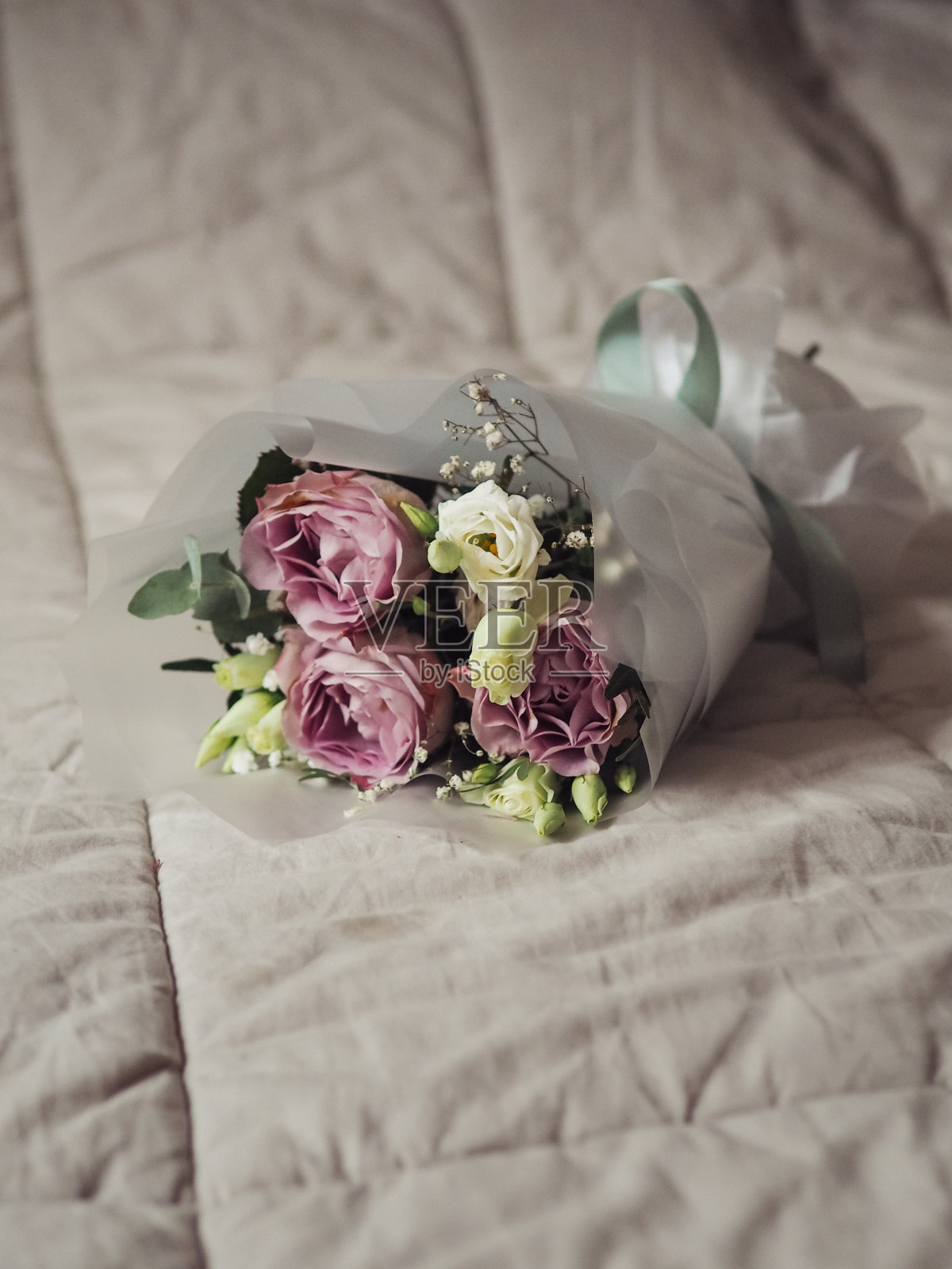 垂直特写的一束紫色和白色的玫瑰，桉树和白色的gypsophila在床上与柔和的毯子。照片摄影图片