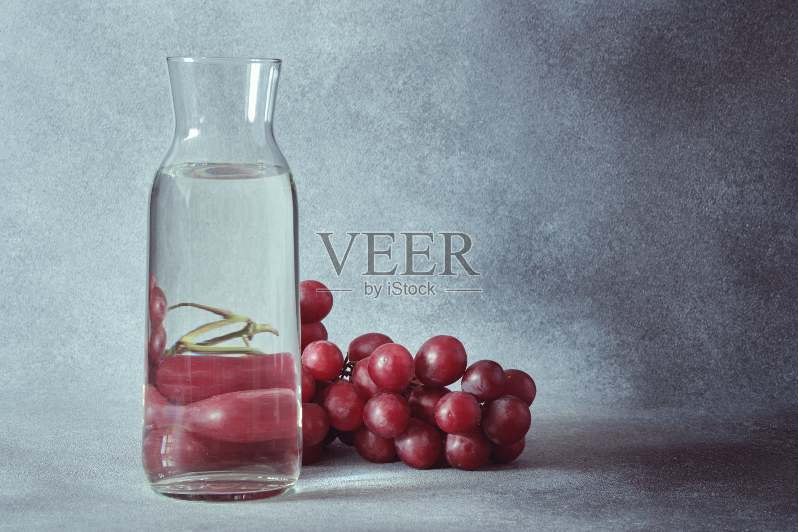 优雅的水玻璃瓶与红葡萄纹理灰色背景照片摄影图片