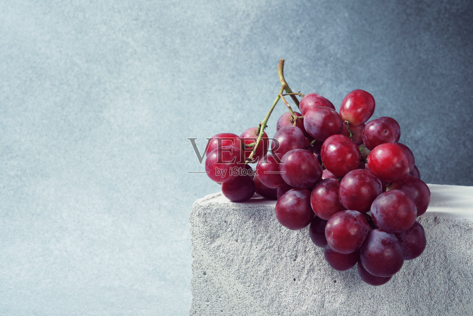 成熟的红葡萄串在灰色背景下的混凝土块上照片摄影图片