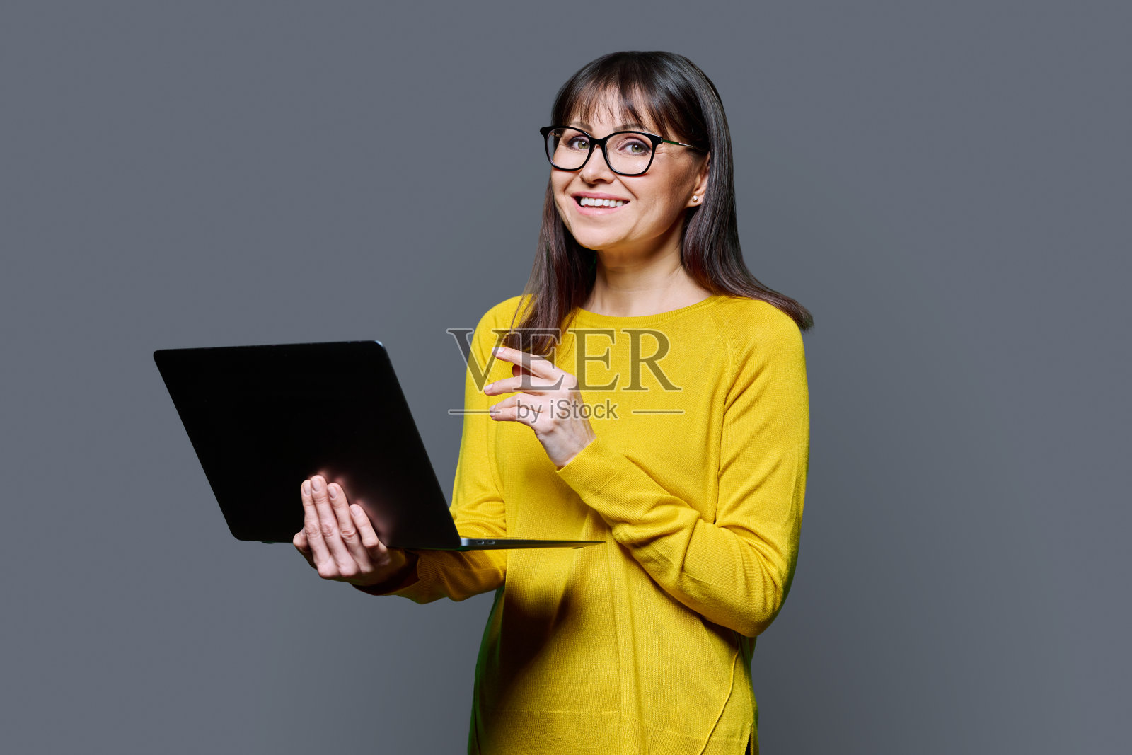 中年妇女在灰色的工作室背景下使用笔记本电脑照片摄影图片