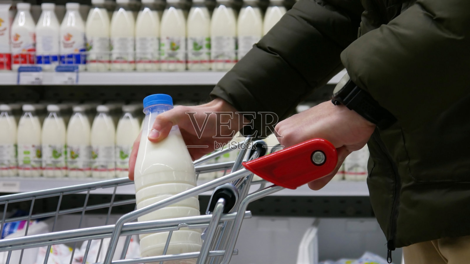奶制品部购物车的特写镜头，一位男顾客把一瓶牛奶放进购物车照片摄影图片