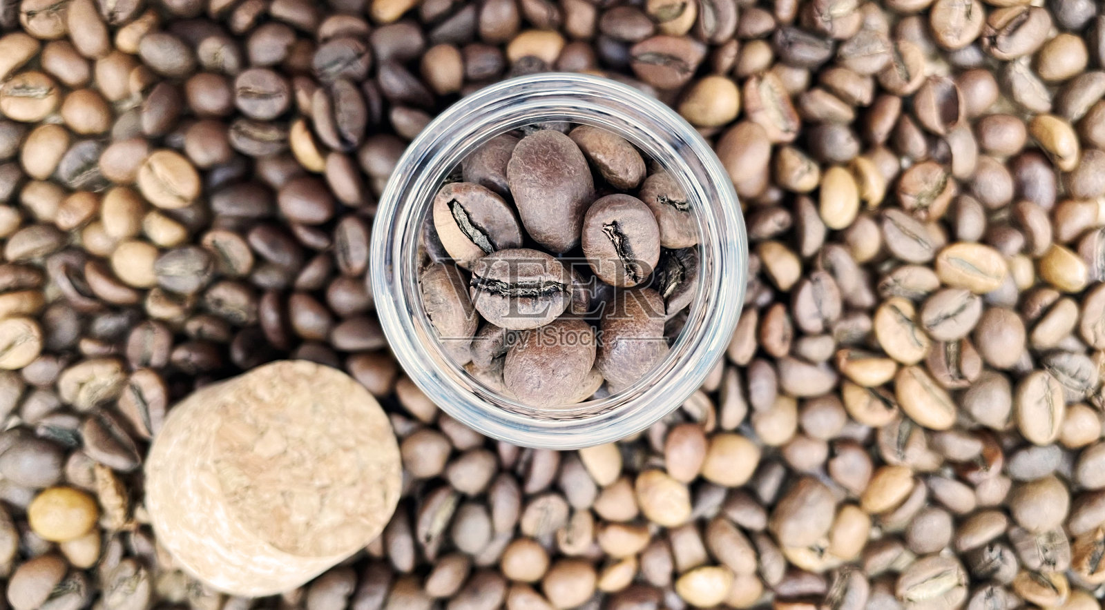 咖啡豆装在一个小玻璃瓶里，用软木盖盖在桌子上。装在透明、密封的储存容器中的咖啡豆。玻璃罐里的咖啡籽。平面布局。照片摄影图片