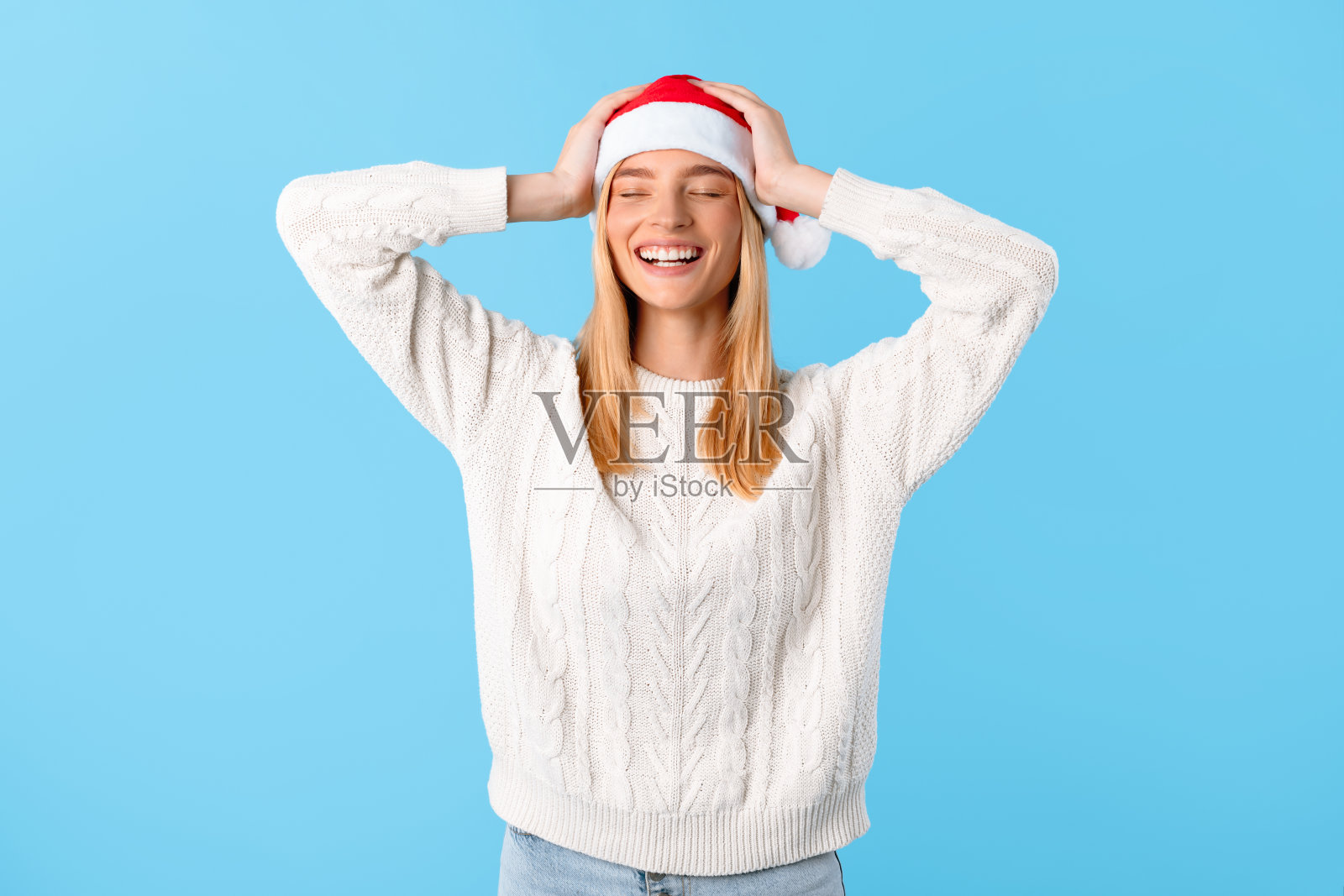 快乐的女人戴着蓝色背景的圣诞老人帽子照片摄影图片