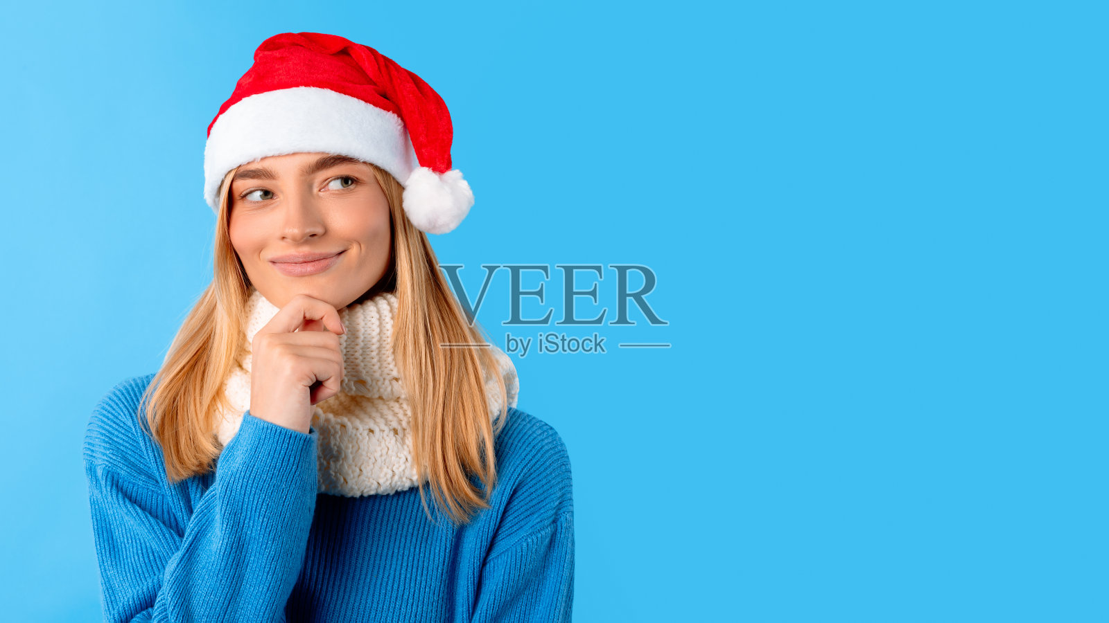 若有所思的女士戴着圣诞帽，抚摸着下巴，看着版面，想着新年庆祝活动和圣诞礼物照片摄影图片