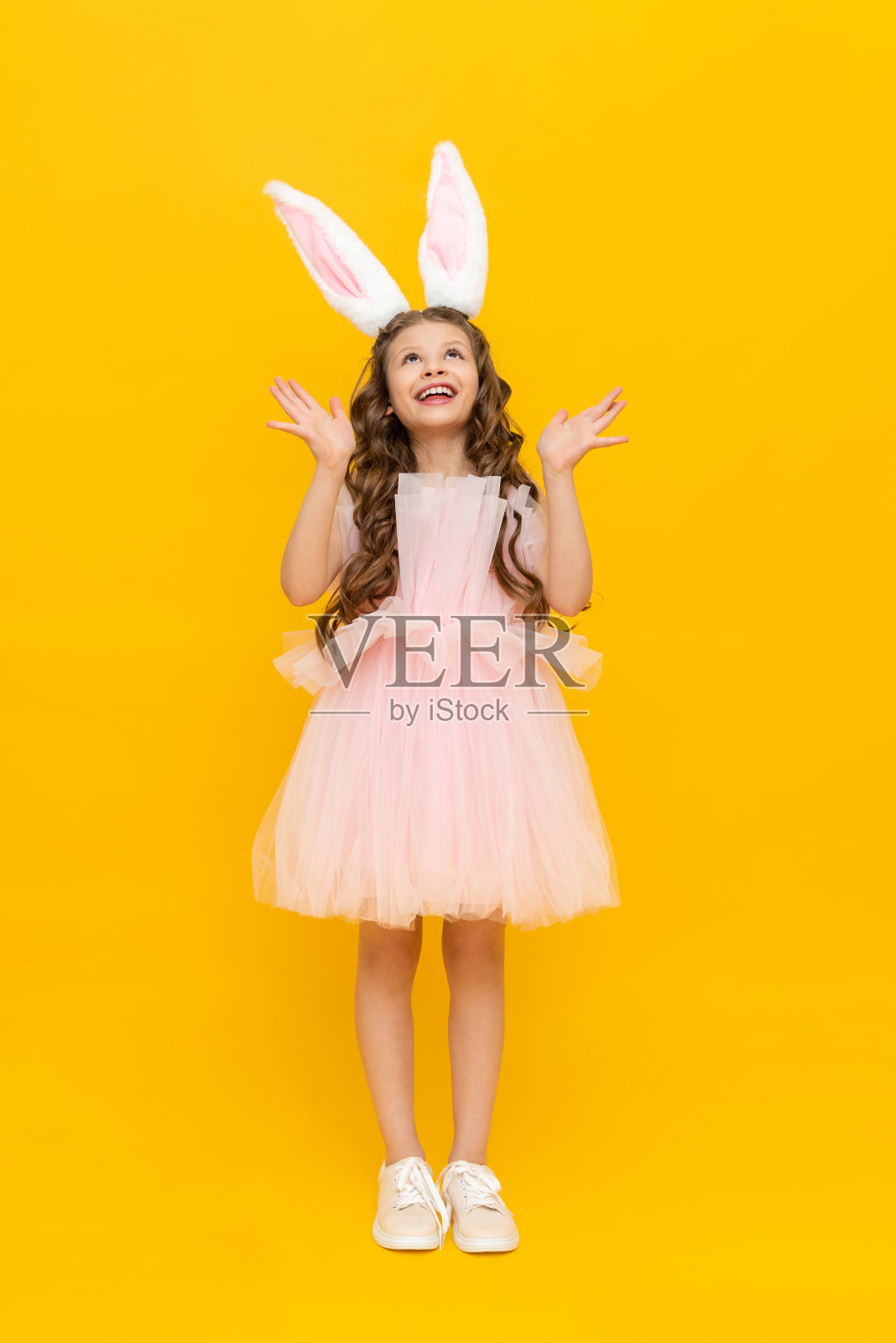 复活节是孩子们的节日。一个十几岁的女孩穿着华丽的衣服，在春天里欢欣鼓舞。这个孩子戴着长长的兔耳。一个美丽的小女孩，一头长发，在黄色孤立的背景上照片摄影图片