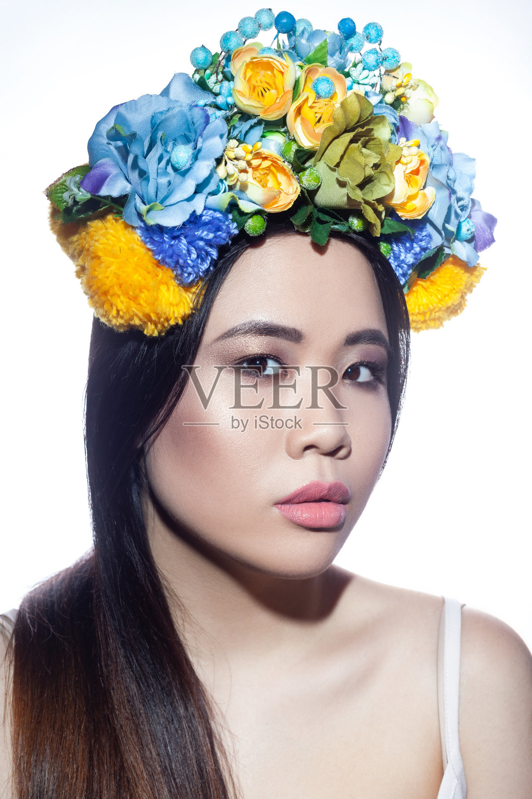 漂亮的女人化着妆，头上顶着花束，表情严肃地看着镜头。照片摄影图片