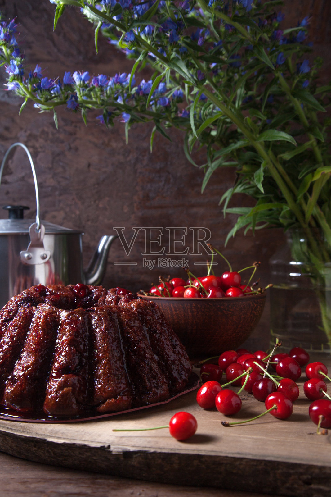 美味的巧克力蛋糕配上甜樱桃，复古水壶和一束蓝色花朵，黑色木制背景。照片摄影图片