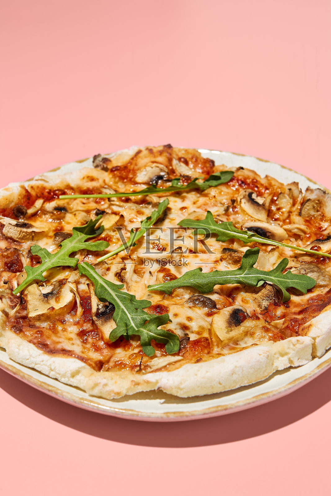 一个无麸质披萨的特写，有蘑菇和西红柿，放在一个时髦的盘子里，背景是粉红色的照片摄影图片