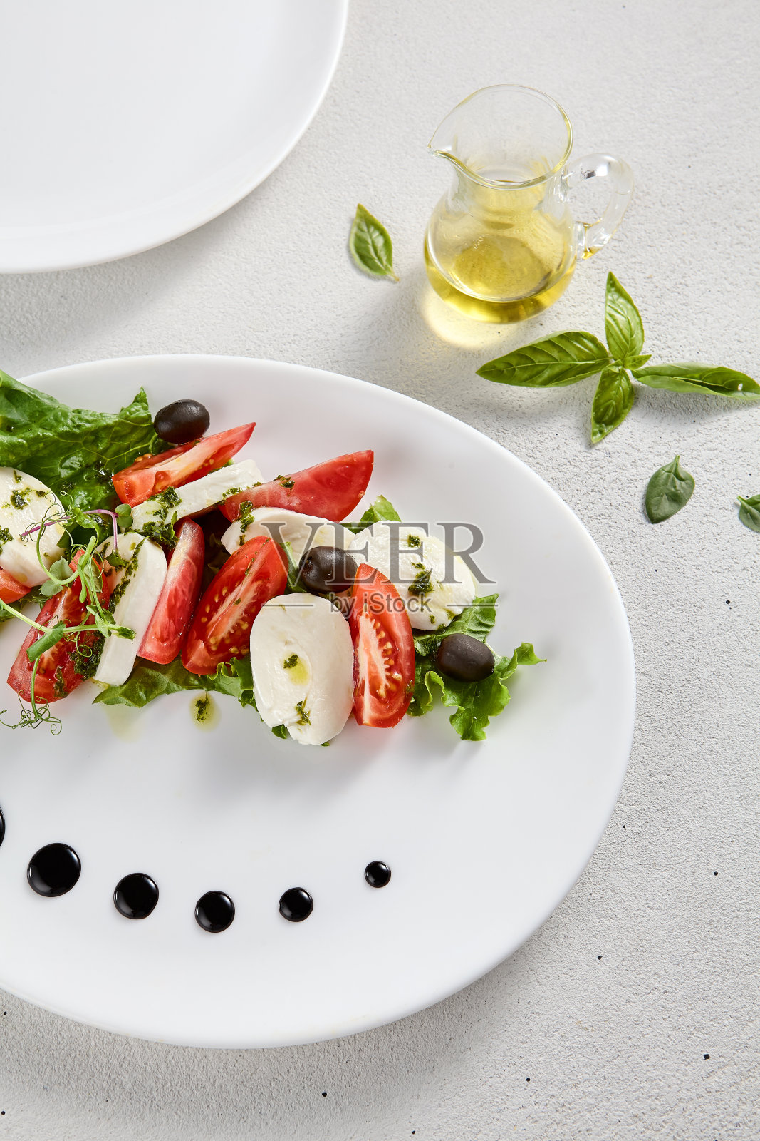 经典的卡普里斯沙拉，配以成熟的西红柿、马苏里拉奶酪和橄榄，配以新鲜的罗勒。适合意大利美食促销和烹饪书籍照片摄影图片