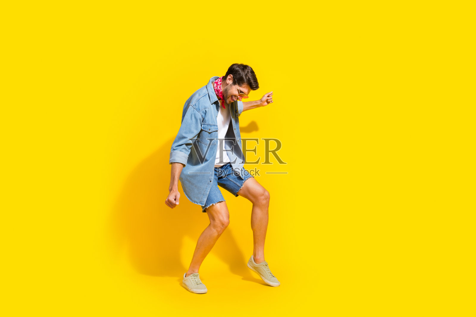 好心情的家伙穿牛仔裤，夹克，短裤，戴着太阳镜，在夏季聚会上跳舞，在明亮的黄色背景孤立照片摄影图片