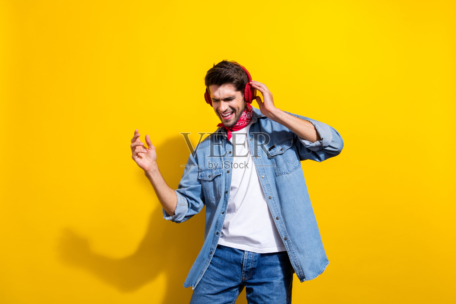 照片肖像英俊的年轻人跳舞，听音乐，触摸耳机穿着时尚的牛仔服装孤立的黄色背景照片摄影图片
