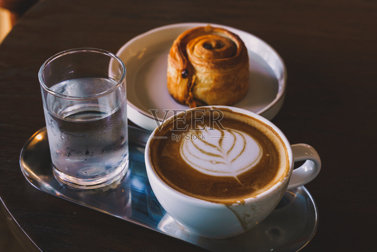 热咖啡拿铁与拉花艺术牛奶泡沫在杯杯和自制葡萄干丹麦白色盘子在木桌子上的顶部视图。在咖啡厅，在咖啡厅，在商务工作期间。照片摄影图片