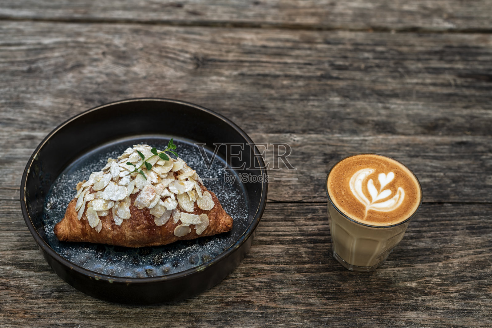 木桌上的热拿铁咖啡和牛角面包。照片摄影图片