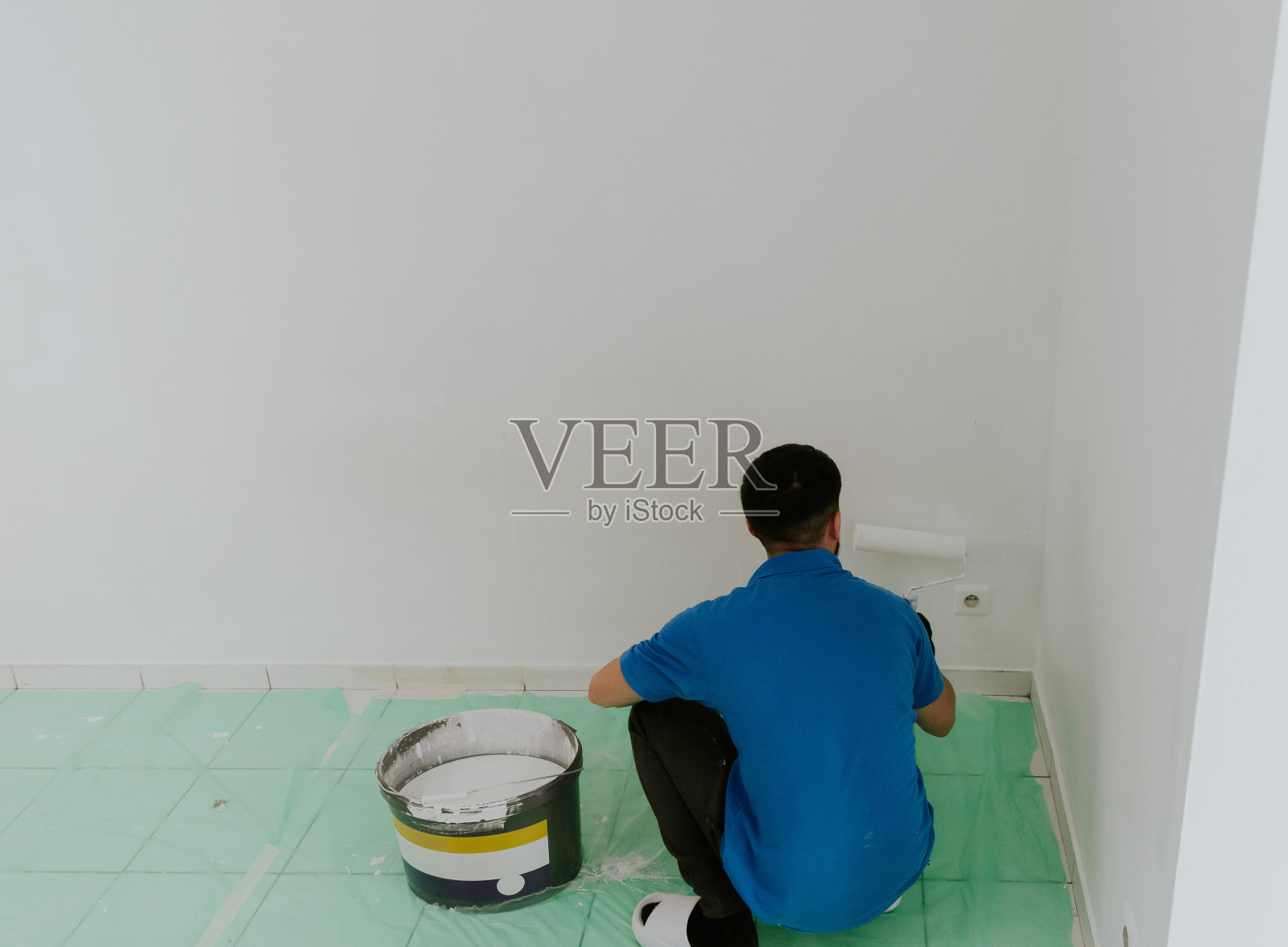 一位年轻的东方男子用滚筒粉刷墙壁照片摄影图片