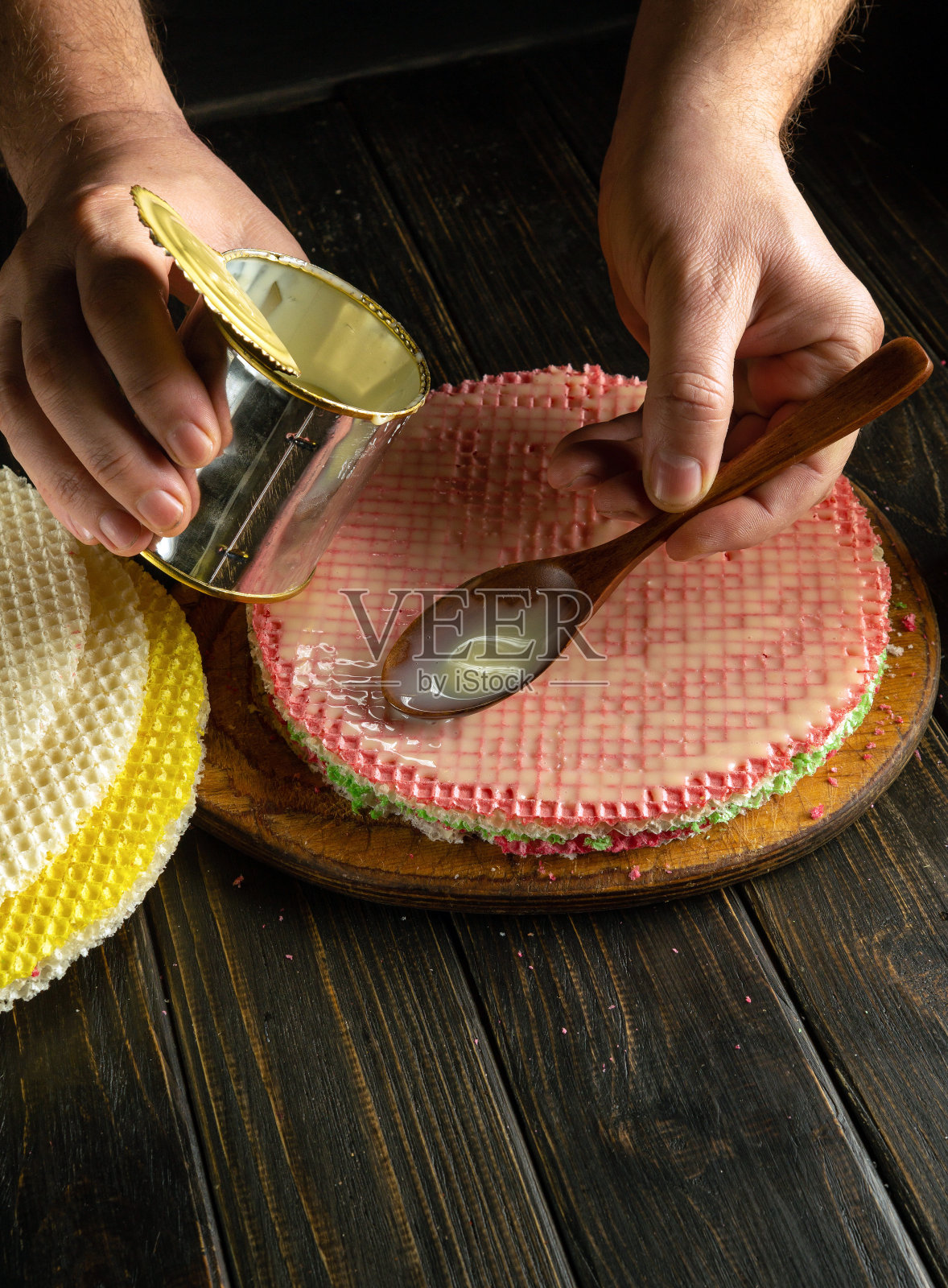 厨师在准备蛋糕的时候，手里拿着一个盛有炼乳的勺子。在餐厅厨房餐桌上准备糕点甜点的概念。照片摄影图片