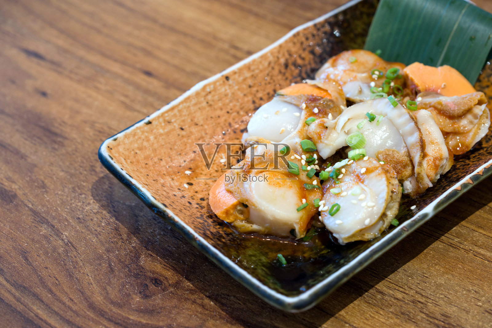 在一家餐馆里，一盘美味的烤扇贝放在一个盘子里，放在一张质朴的木桌上。照片摄影图片