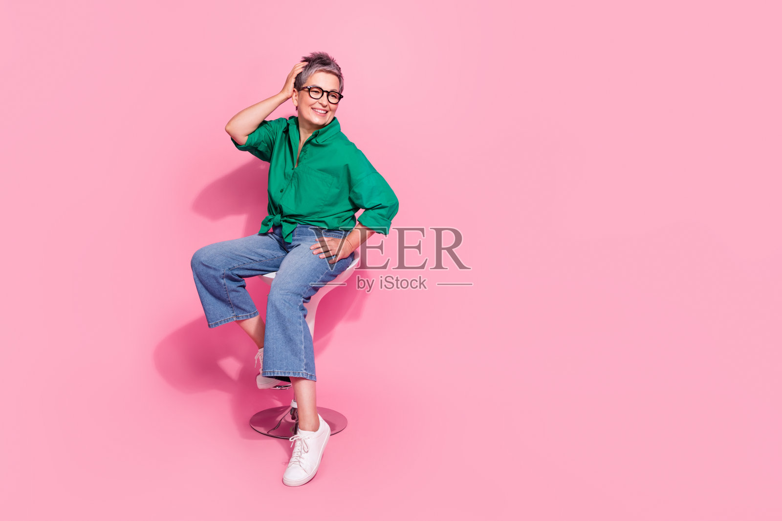 满意的女人全身照片穿着绿色衬衫触摸新发型在美容院坐在凳子上孤立的粉红色背景照片摄影图片