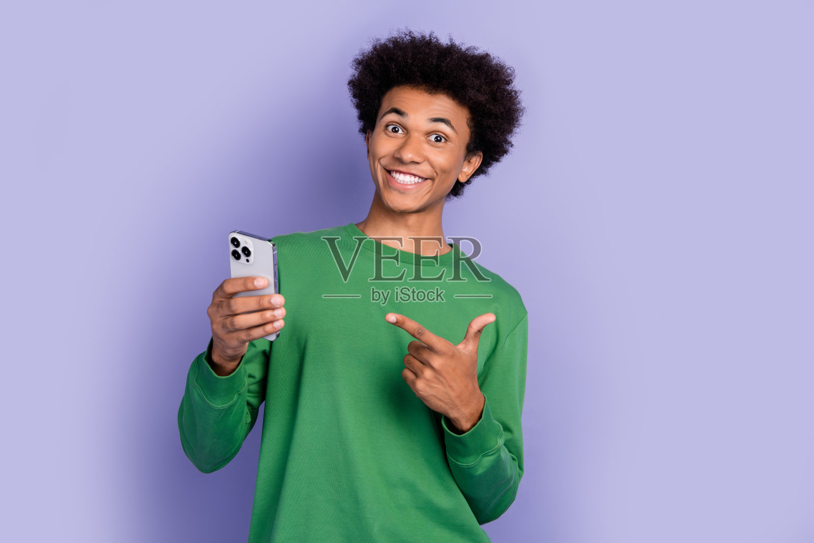 照片中心情愉快的家伙穿着绿色的套头衫，显示手指现代装置孤立的紫色背景照片摄影图片