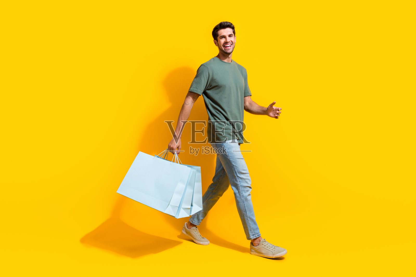 穿着卡其布t恤的兴奋开朗的男子手持便宜货的全身照片，孤立的黄色背景照片摄影图片