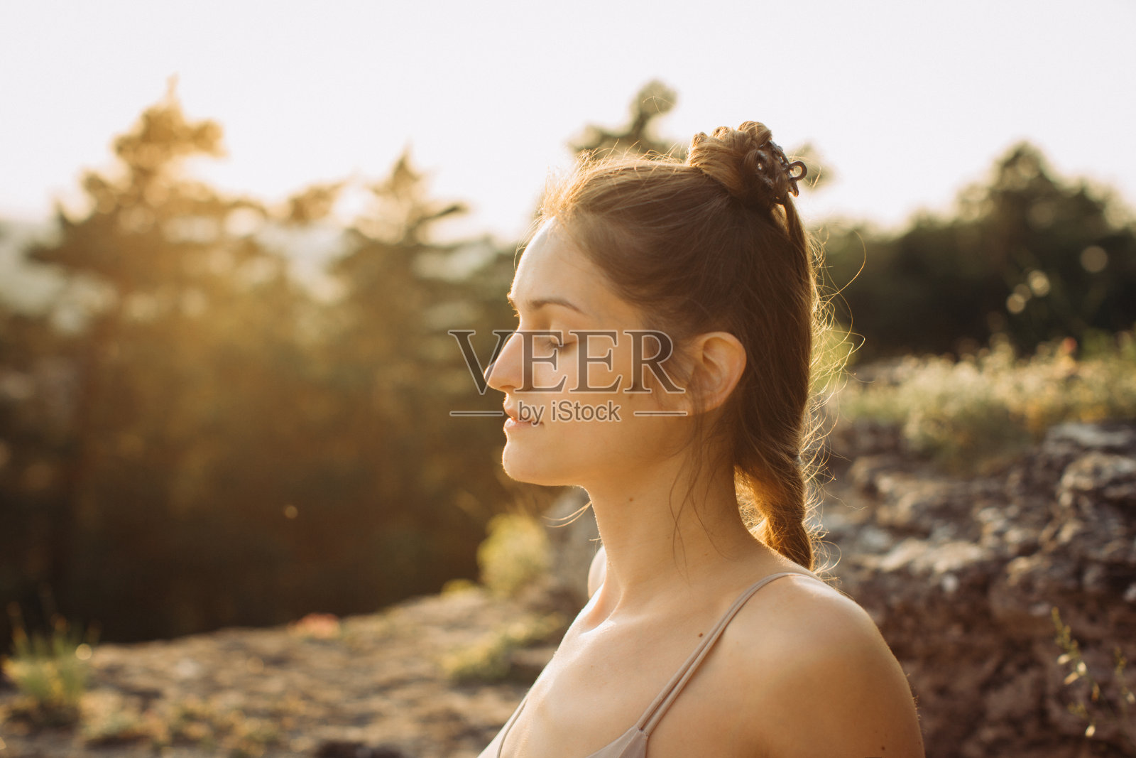 夕阳下，一位年轻女子在松林中沉思。健康的生活方式，享受自然。照片摄影图片