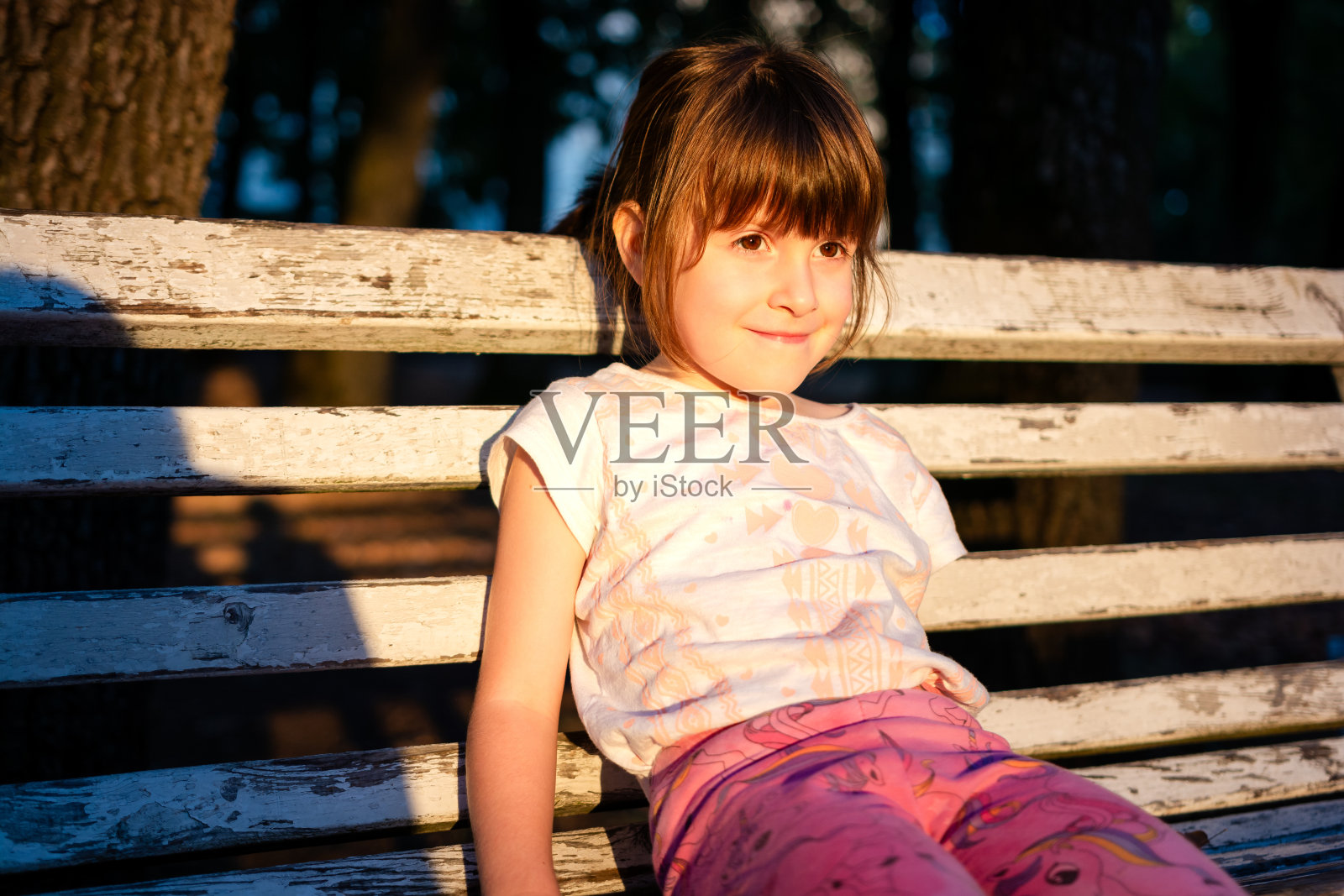 可爱快乐的女孩坐在公园的长椅上照片摄影图片