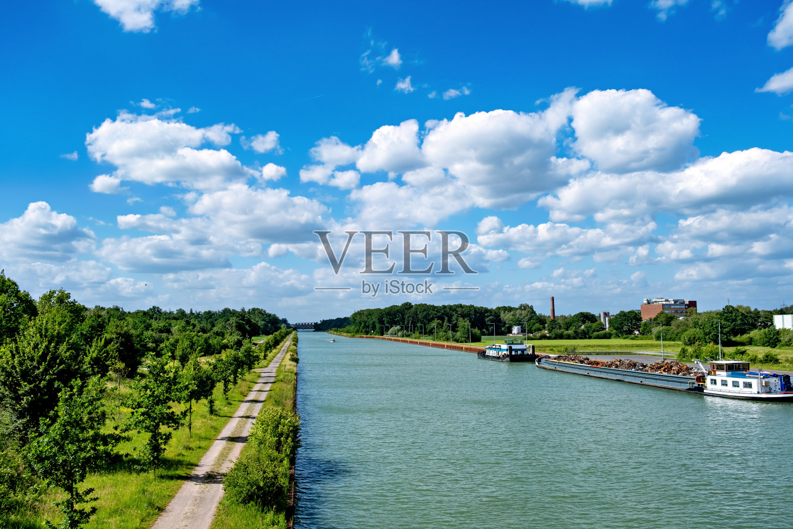 在德国运河的码头上，船和装满废金属的驳船停在那里。照片摄影图片