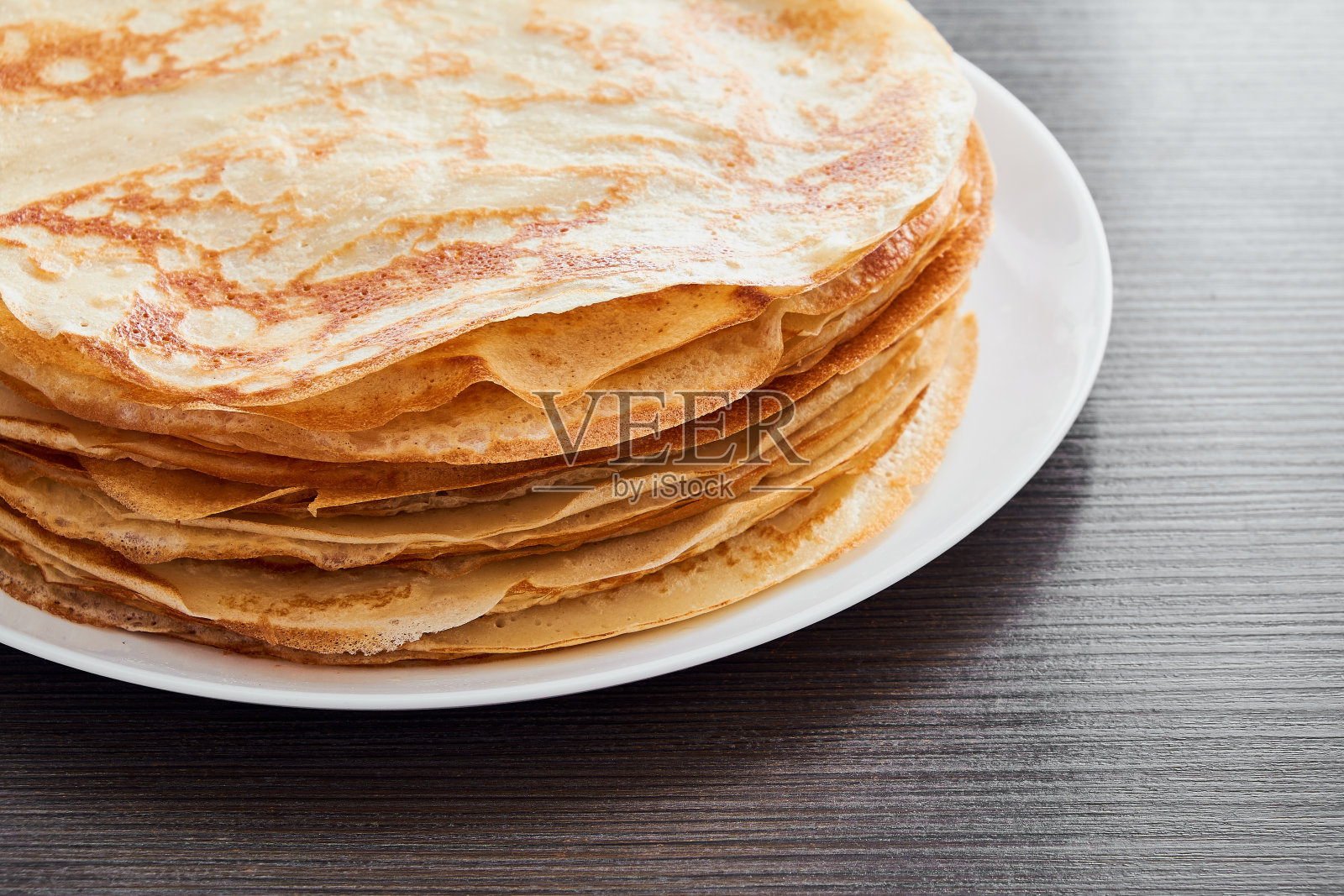 一个圆形的盘子，上面放着煎薄饼，放在棕色的桌子上。早餐吃甜点。阳光明媚的早晨。照片摄影图片
