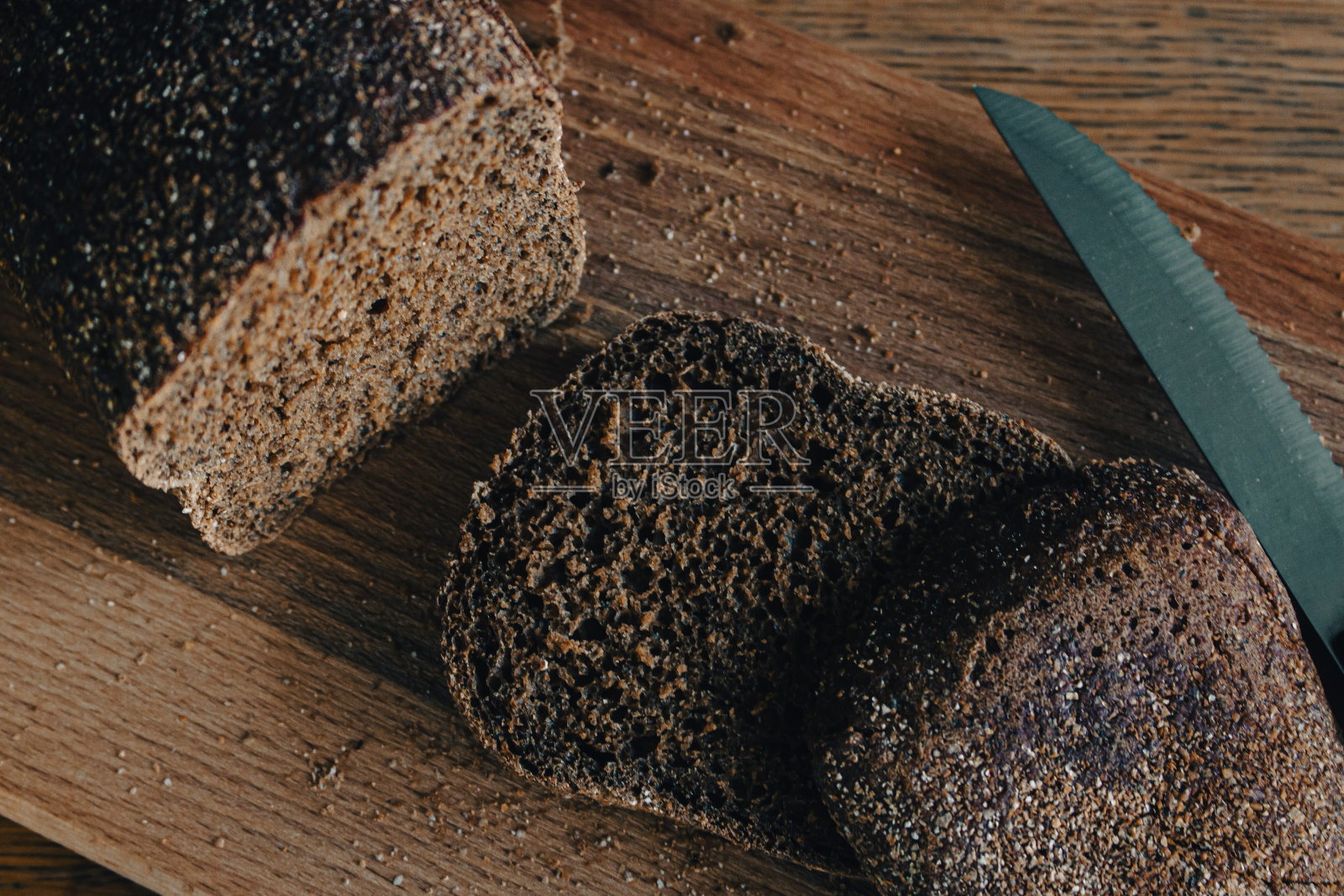 木板上有刀的灰色面包。小麦面包切片放在砧板上。烘焙产品。桌上的硬皮谷物面包。晚餐的概念。健康的饮食生活方式。新鲜的谷物面包。照片摄影图片