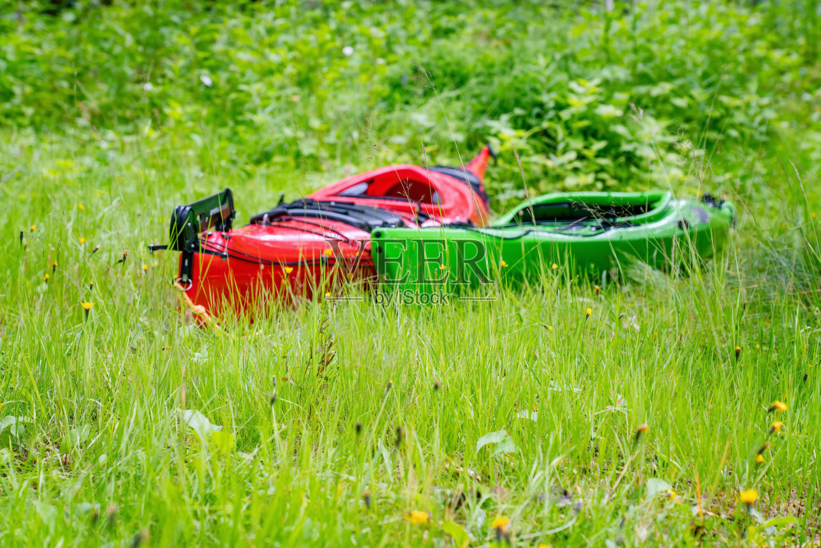 两只故意模糊的皮划艇——红色的和绿色的在绿草地上。近距离低空照片。前景草对焦照片摄影图片