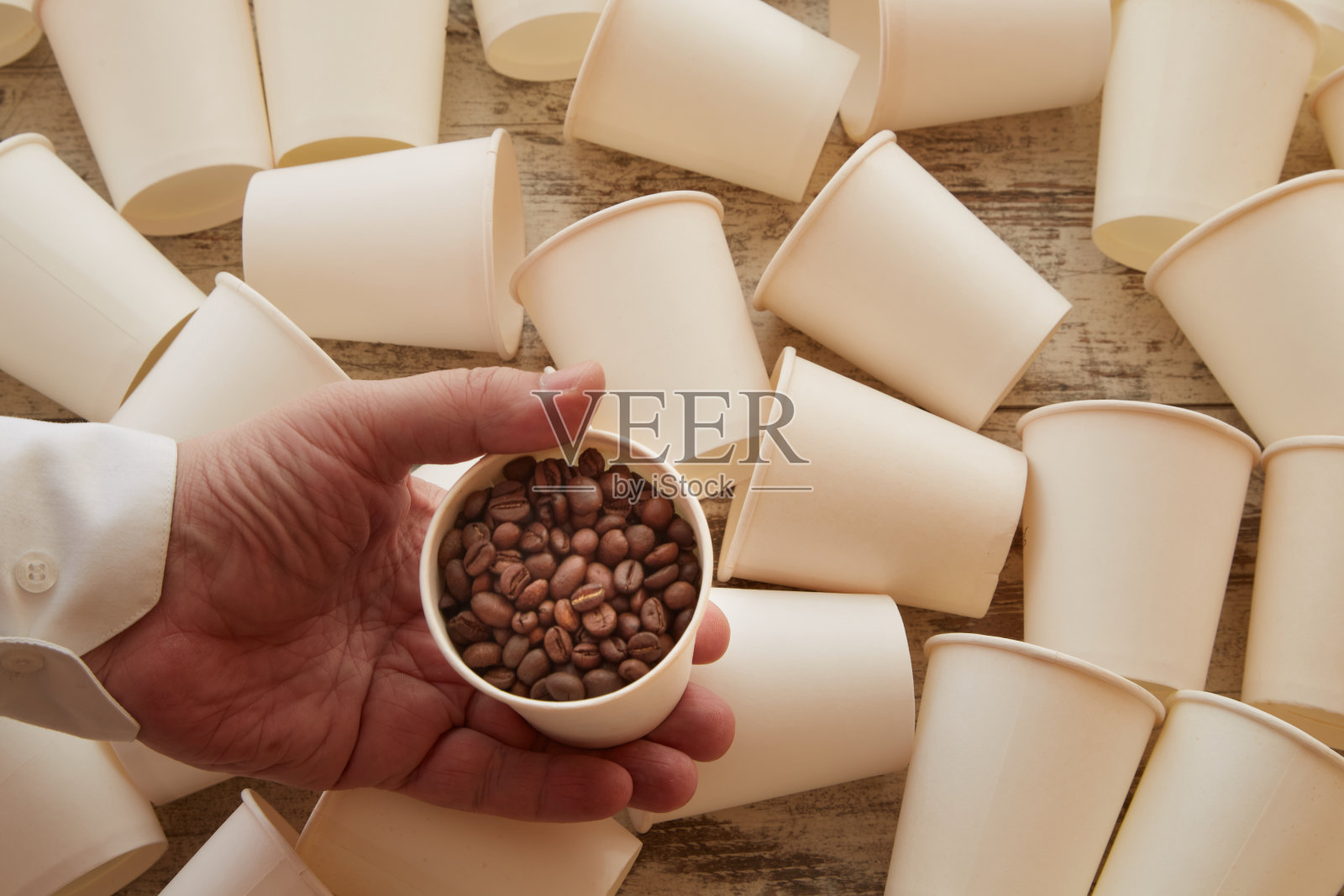 一只手在空杯子中拿着一个装有咖啡豆的纸杯。新鲜的咖啡豆，捐赠给咖啡照片摄影图片