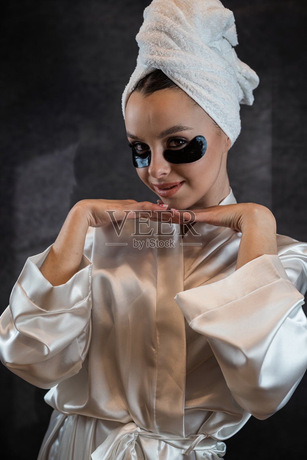 年轻美丽的女士在毛巾上涂抹胶原蛋白黑色贴片，在眼睛下面隔离黑色照片摄影图片