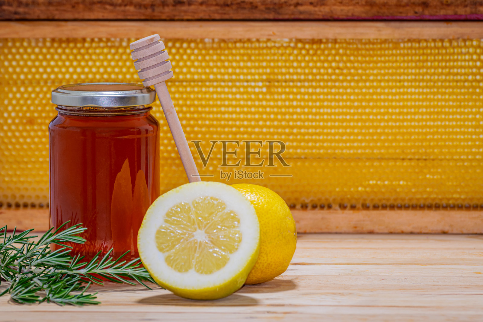 带分配器的蜂蜜罐，一个迷迭香和一个半柠檬放在木头上，背景是蜂巢照片摄影图片